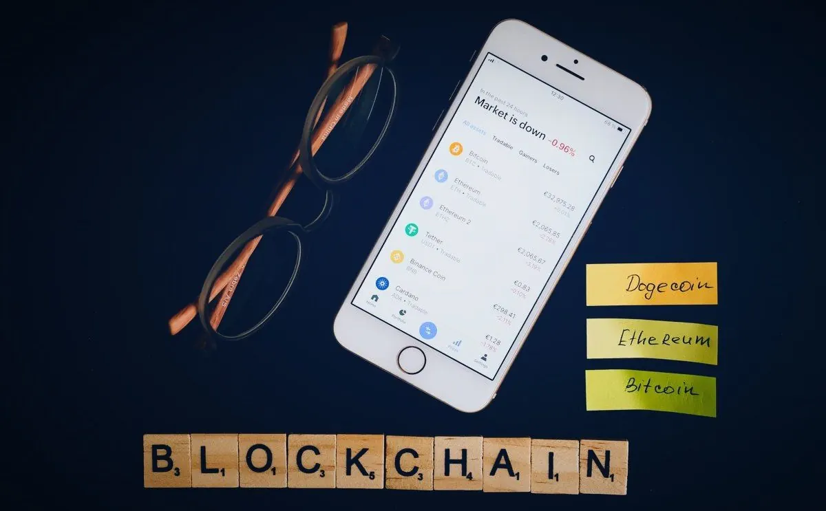 Téléphone affichant des cours de cryptos dont le stablecoin Tether, à côté du mot BLOCKCHAIN en lettres de bois
